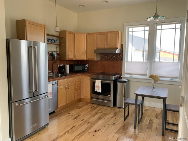 kitchen featuring a sink, under cabinet range hood, light wood-style flooring, dark countertops, and appliances with stainless steel finishes