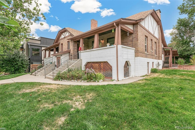 view of front of house featuring brick siding, stairway, a chimney, and a front yard