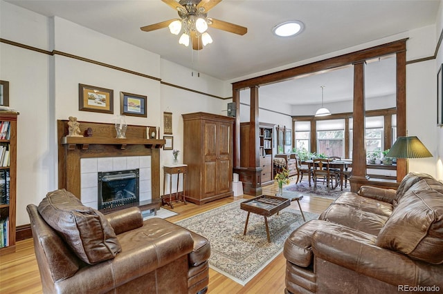 living room with a fireplace, light wood-type flooring, and ceiling fan