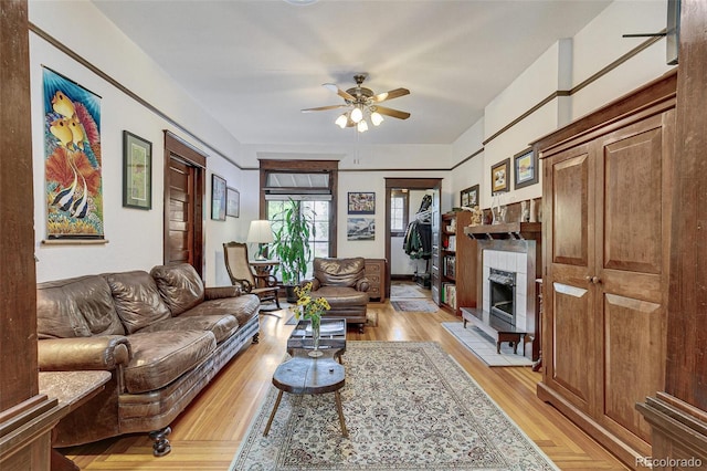 living area with a fireplace, light wood-style floors, and a ceiling fan