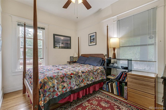 bedroom featuring ceiling fan, baseboards, multiple windows, and wood finished floors