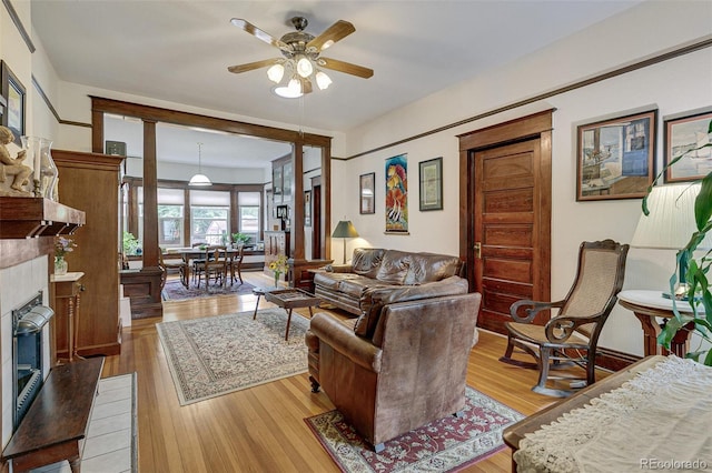 living area with a glass covered fireplace, light wood-style flooring, and ceiling fan