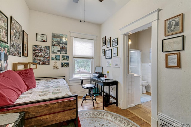 bedroom with connected bathroom, tile walls, a ceiling fan, and wood finished floors