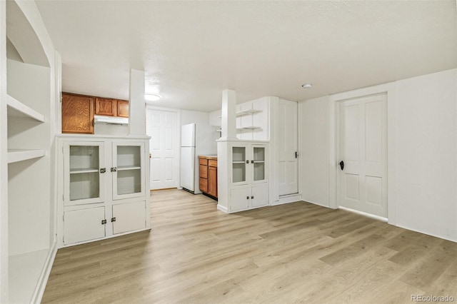 kitchen with brown cabinetry, light wood-type flooring, and freestanding refrigerator