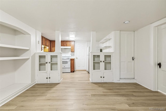 kitchen featuring under cabinet range hood, built in features, light wood-style flooring, brown cabinetry, and white appliances