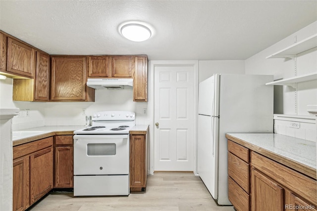 kitchen with white appliances, light countertops, brown cabinets, and under cabinet range hood