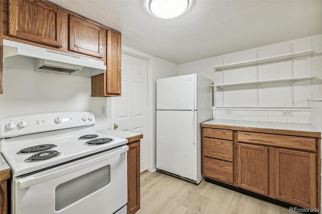 kitchen with white appliances, brown cabinetry, under cabinet range hood, and light countertops