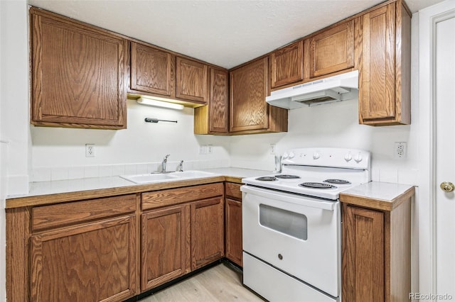 kitchen with under cabinet range hood, electric range, light countertops, and a sink