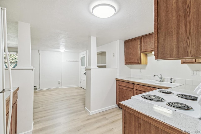 kitchen with baseboards, light wood-type flooring, light countertops, brown cabinetry, and a sink