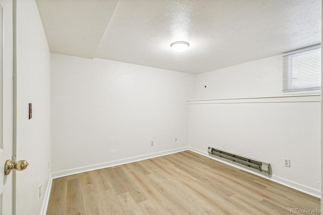 unfurnished room with a baseboard radiator, a textured ceiling, baseboards, and wood finished floors