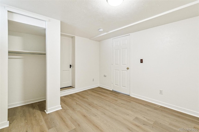 unfurnished bedroom with a closet, a textured ceiling, baseboards, and wood finished floors