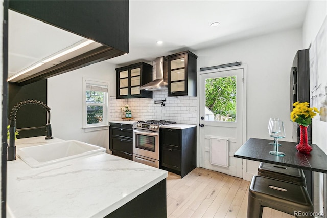 3625 W 9th Ave, Denver, CO 80204 - kitchen with wall chimney range hood, stainless steel range with gas cooktop, a sink, light wood-style floors, and dark cabinetry