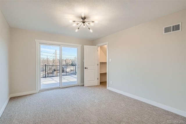 unfurnished room with visible vents, a textured ceiling, an inviting chandelier, baseboards, and light colored carpet