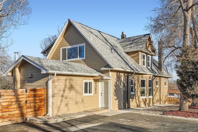 view of front of home with a shingled roof, a chimney, and fence