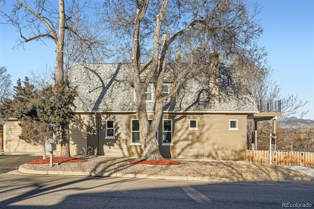 view of front of home with brick siding, roof with shingles, and fence