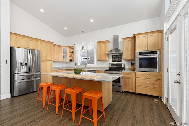 kitchen featuring a center island, dark wood-type flooring, stainless steel appliances, wall chimney range hood, and a kitchen breakfast bar