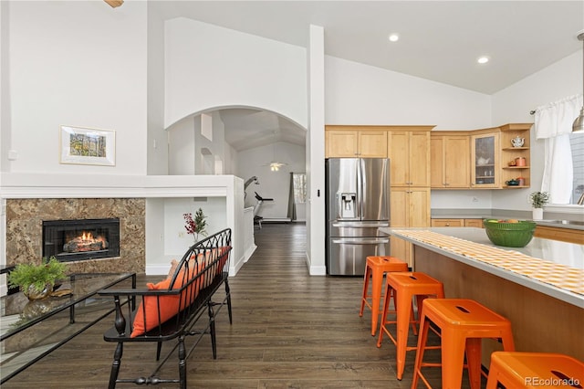 kitchen featuring light brown cabinets, dark wood-type flooring, a premium fireplace, high vaulted ceiling, and stainless steel fridge