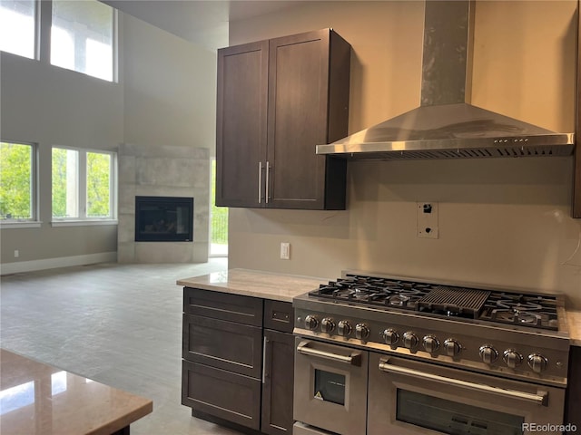 485 Cardiff Cir, Colorado Springs, CO 80906 - kitchen featuring wall chimney exhaust hood, double oven range, light stone counters, dark brown cabinets, and a tile fireplace