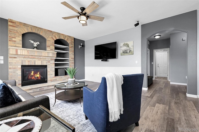 4069 Copper Ct, Castle Rock, CO 80104 - living area with built in shelves, arched walkways, a ceiling fan, wood finished floors, and a brick fireplace