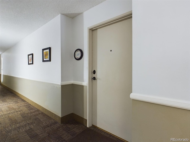 hall with dark carpet and a textured ceiling