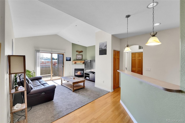 living room with lofted ceiling, light wood-style flooring, baseboards, and a tile fireplace