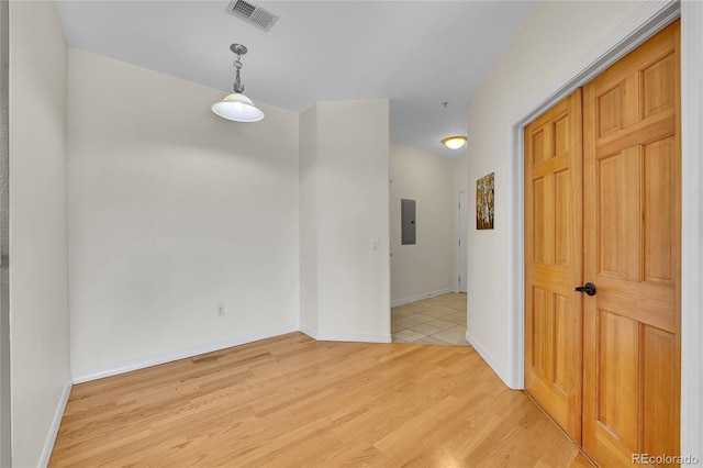 spare room featuring electric panel, visible vents, baseboards, and light wood finished floors