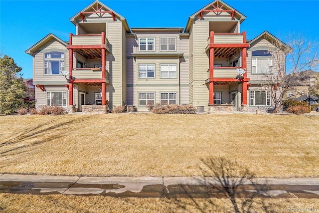 view of front of property featuring a front yard, a balcony, and cooling unit