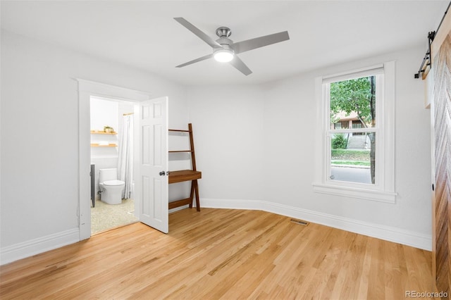 2995 Yates St, Denver, CO 80212 - unfurnished bedroom with a barn door, light wood-style flooring, connected bathroom, and a ceiling fan