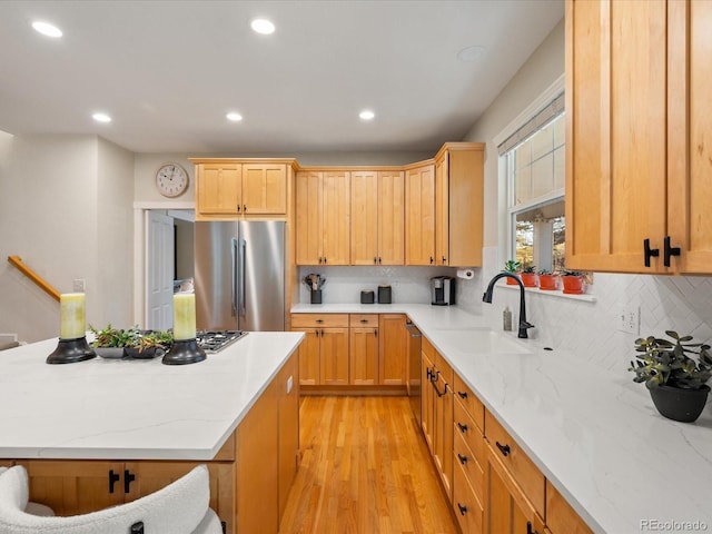 kitchen with light stone countertops, sink, stainless steel appliances, backsplash, and light hardwood / wood-style floors