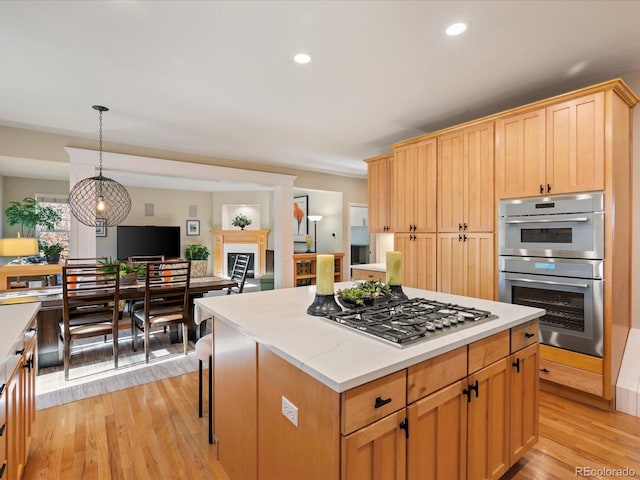 kitchen with a kitchen bar, appliances with stainless steel finishes, light hardwood / wood-style floors, a kitchen island, and hanging light fixtures