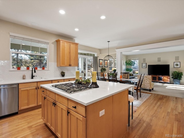 kitchen featuring sink, a center island, hanging light fixtures, appliances with stainless steel finishes, and light wood-type flooring