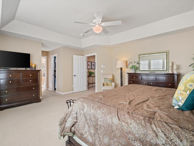 bedroom with a raised ceiling, a walk in closet, ceiling fan, and light carpet