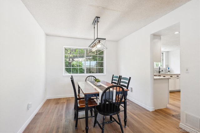 7822 W Ottawa Pl, Littleton, CO 80128 - dining area featuring light wood-style floors, baseboards, a textured ceiling, and a chandelier