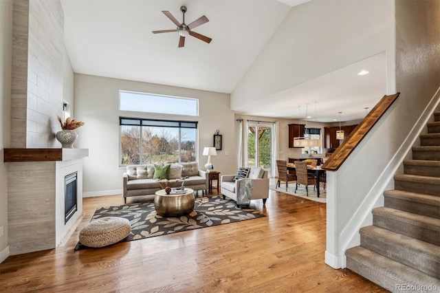 living room featuring ceiling fan, light hardwood / wood-style floors, a fireplace, and high vaulted ceiling