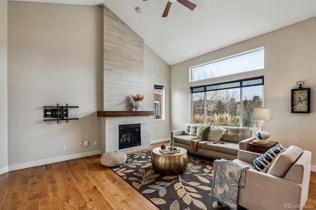 living room featuring a tiled fireplace, ceiling fan, hardwood / wood-style floors, and high vaulted ceiling