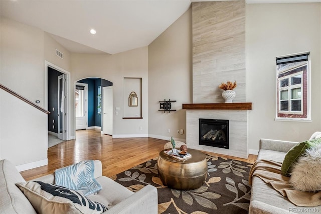 living room with a tile fireplace, wood-type flooring, and high vaulted ceiling