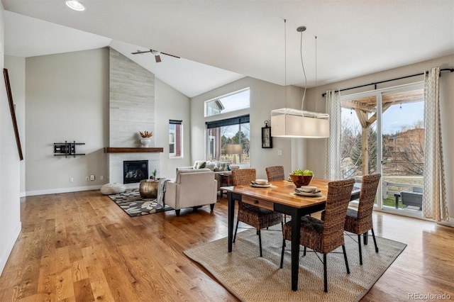 dining area with high vaulted ceiling, a fireplace, a wealth of natural light, and light hardwood / wood-style flooring