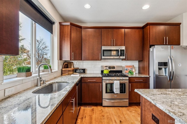 kitchen with light stone countertops, sink, backsplash, appliances with stainless steel finishes, and light wood-type flooring