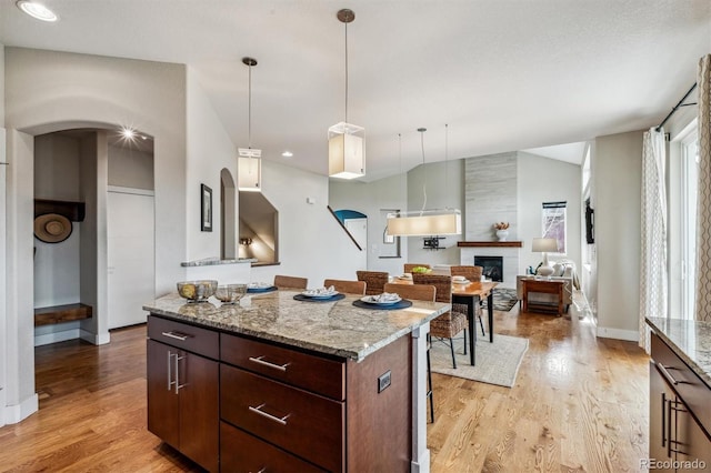 kitchen featuring light stone counters, dark brown cabinets, a fireplace, a center island, and light hardwood / wood-style floors