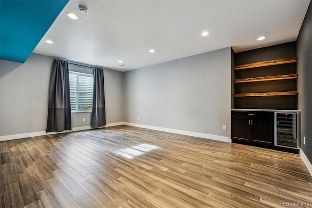 unfurnished living room with a textured ceiling, light hardwood / wood-style floors, and beverage cooler