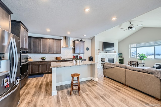 kitchen with a center island, a breakfast bar, stainless steel appliances, open floor plan, and wall chimney exhaust hood