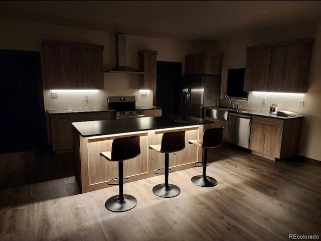 104 Dotson St, Manassa, CO 81141 - kitchen featuring stainless steel appliances, wall chimney range hood, a kitchen island, a breakfast bar, and light wood-style flooring