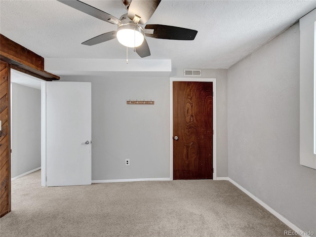 unfurnished room featuring visible vents, carpet flooring, a textured ceiling, and a ceiling fan