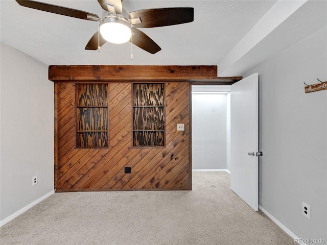 carpeted spare room with wood walls, baseboards, and a ceiling fan