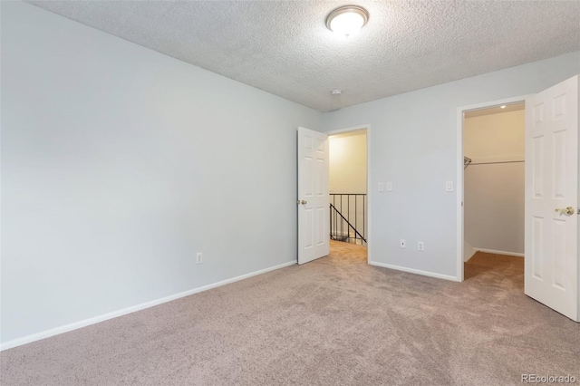 unfurnished bedroom featuring a walk in closet, a closet, carpet floors, and a textured ceiling