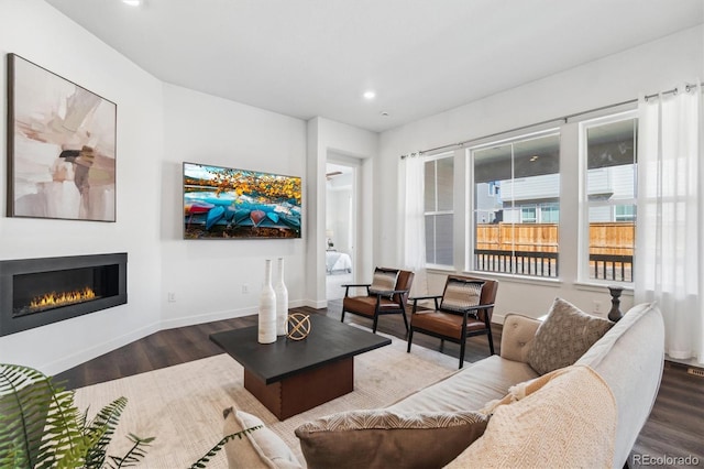 living room featuring a glass covered fireplace, recessed lighting, baseboards, and wood finished floors