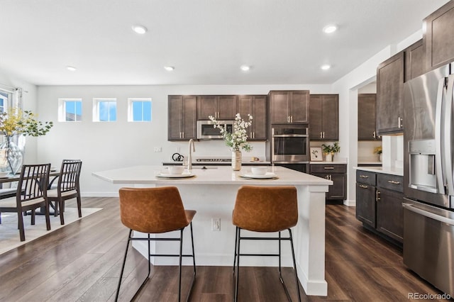 kitchen with stainless steel appliances, light countertops, a kitchen breakfast bar, and dark wood-style floors