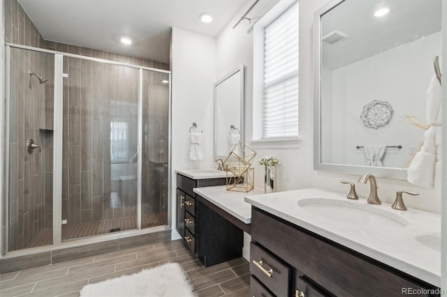 bathroom with a stall shower, visible vents, a sink, wood finish floors, and two vanities