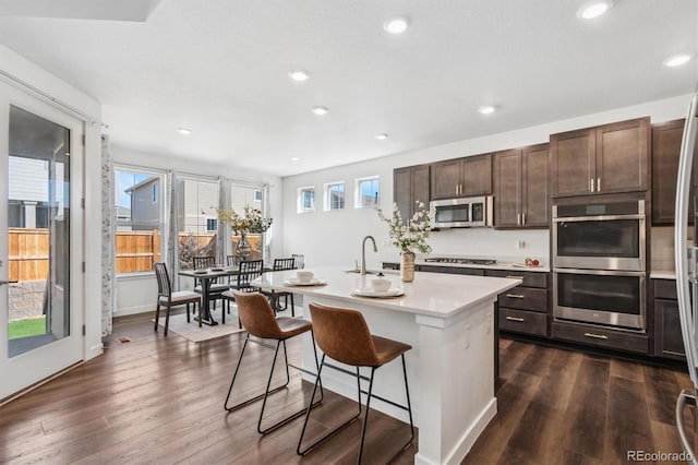 kitchen featuring stainless steel appliances, a center island with sink, dark wood finished floors, and light countertops