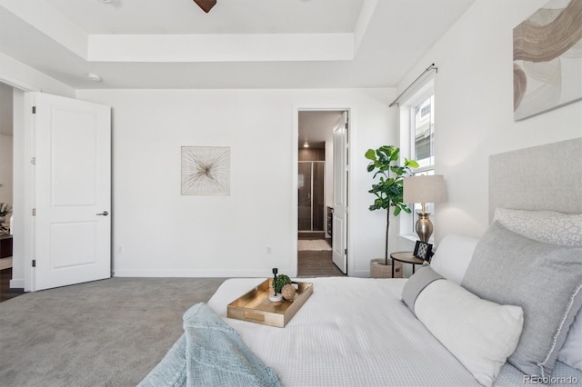 carpeted bedroom featuring a tray ceiling, baseboards, and ensuite bath